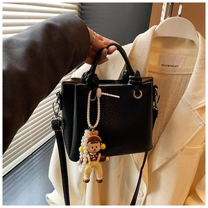 Detail of black textured bucket bag with cute cartoon doll and pearl chain decoration