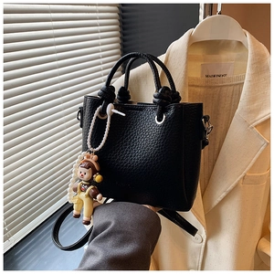 Detail of black lychee grain bucket bag featuring knot handle and cartoon doll charm