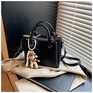 Detail of black litchi pattern leather bucket bag with cute cartoon doll charm