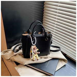 Detail of black lychee texture leather bucket bag with pearl cartoon girl charm on beige coat