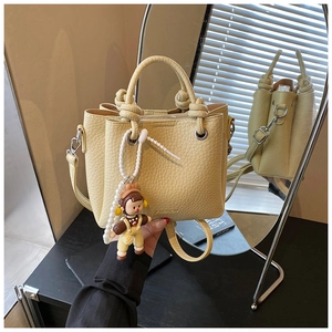 Detail of yellow pebbled leather bucket bag with knotted handle and pearl doll charm