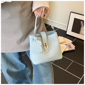 Détail du sac seau en cuir bleu clair à motif litchi avec pendentif chien et boucle en métal