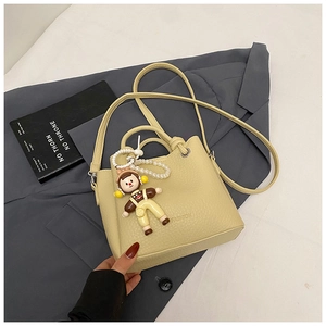 Detail of light yellow bucket bag with lychee texture and pearl pendant on a grey blazer
