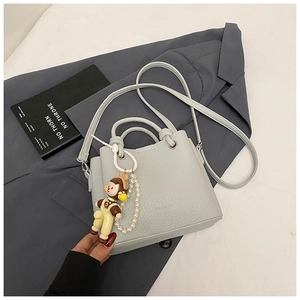 Close-up of pebble leather bucket bag with fashion logo, pearl chain, and cute charm