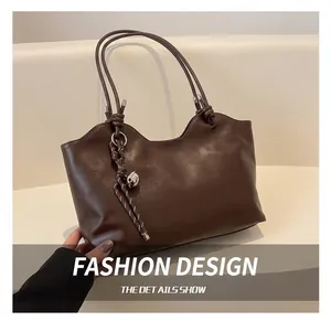 Detail of dark brown tote bag with wavy rim, smooth texture and silver bell charm