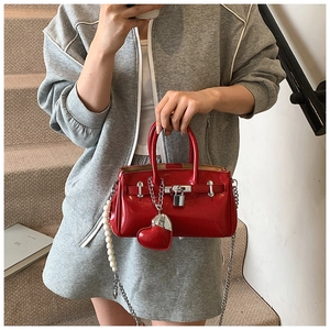 Detail of red patent leather handbag with silver lock and decorative pearl strap accessory