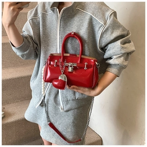 Detail of red glossy mini handbag with pearl chain and silver padlock on stairs