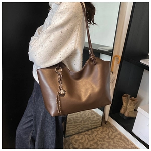 Detail of a large dark brown faux leather tote bag with braided tassel and metal ball charm