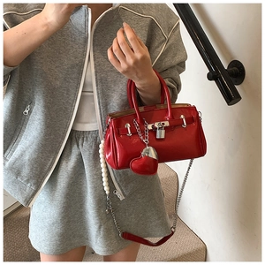 Detail of red patent leather handbag featuring pearl chain and heart-shaped charm
