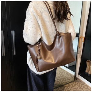 Deep brown tote bag detail showing knotted shoulder strap and metal ball charm pendant