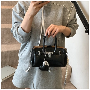 Detail of glossy black handbag featuring silver buckle, pearl strap, and heart charm