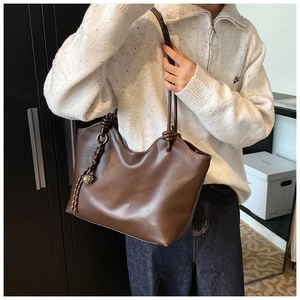 Detail of a dark brown PU leather tote bag with a unique knot shoulder strap and metal charm