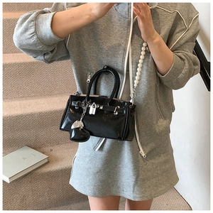 Detail of black patent leather Kelly bag with pearl shoulder strap and silver heart charm