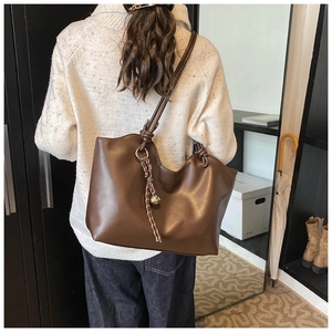 Detail of large dark brown leather tote bag with woven knot and silver metal pendant