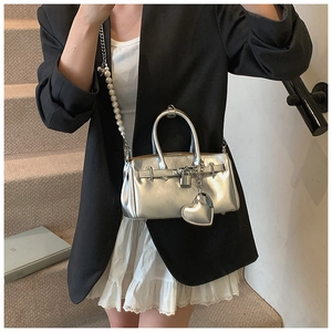 Detail of silver metallic Kelly bag with pearl strap and heart pendant on shoulder