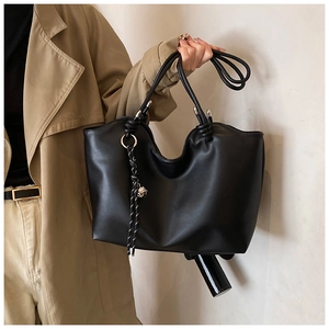Detail of black leather tote bag with unique knotted strap and woven tassel charm