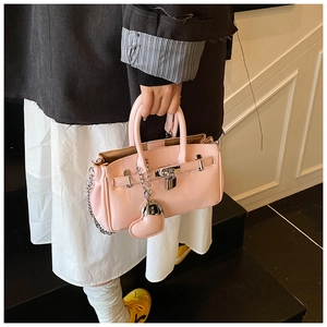 Detail of pink fashion handbag with silver lock and heart charm in street style view