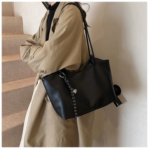 Detail of black leather tote bag with braided cord and gold metal ring on beige coat