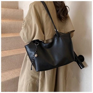 Detail of a large black tote bag with slim straps and a metallic bell pendant charm