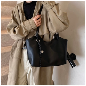 Detail of black tote bag with knot strap and bell charm shown on model in studio