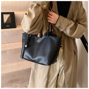 Detail of black leather tote bag featuring wavy top edge and decorative knotted charm