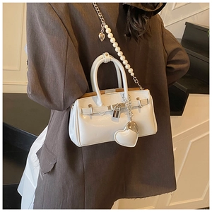 Close-up of white glossy tote with heart charm and pearl chain strap detail