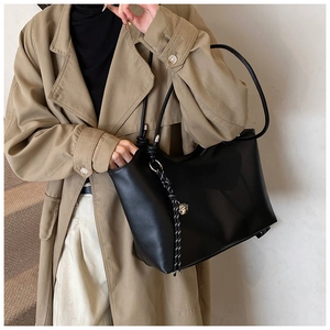 Detail of a black large tote bag with silver bell charm and woven rope on long trench coat
