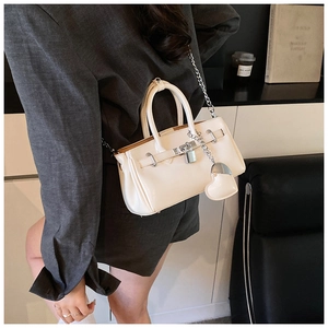 Detail of cream leather shoulder bag with silver lock and heart charm in a lifestyle setting