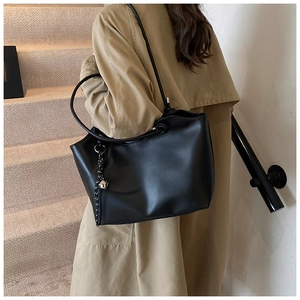 Detail of a black leather tote bag with silver bell charm worn over a beige trench coat