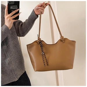 Detail of brown faux leather tote bag featuring a wavy edge and striped ribbon on handle