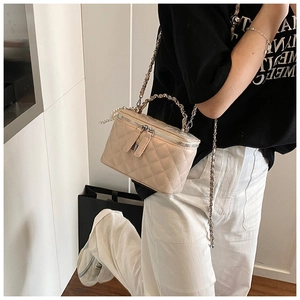 Detail van beige gewatteerde vanity tas met parelketting en metalen handvat op model