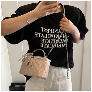 Detail van luxe champagne vanity bag met gewatteerd leer en een hanger met parelkwastjes