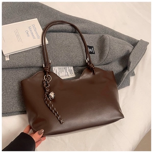 Detail of a dark brown large tote bag with smooth texture and bell charm accessory