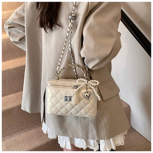 Detail van witte gewatteerde box-tas met parelmoer strik en hartvormige hanger aan ketting
