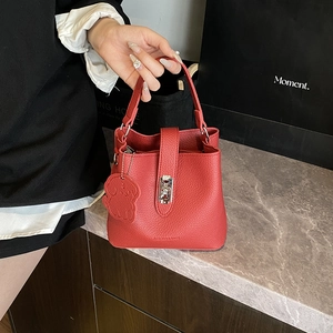 Sac seau rouge texture litchi avec fermoir rotatif argenté porté par une personne