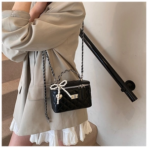 Detail van zwarte gewatteerde box-tas met parelstrik en metalen hartvormige hanger