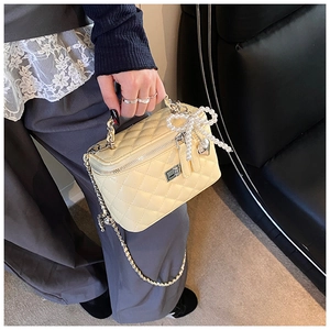 Detail van gele gewatteerde tas met parelstrik en hartvormige hanger goud
