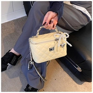 Detail van crème gewatteerde handtas met parelstrikn en zilveren hartvormige hanger