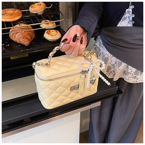 Detail van een gewatteerde gele box-tas met kettinghandvat en parelmoer strikhanger decor