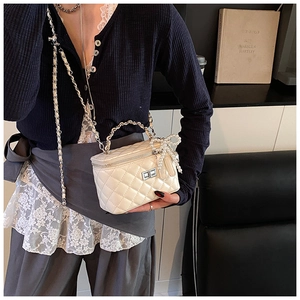 Detail van witte gewatteerde mini-tas met parelmoeren strik en zilveren ketting