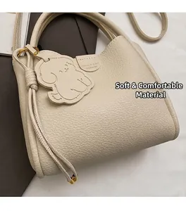 Detail of cream pebbled leather bucket bag with dog-shaped charm and brand embossing