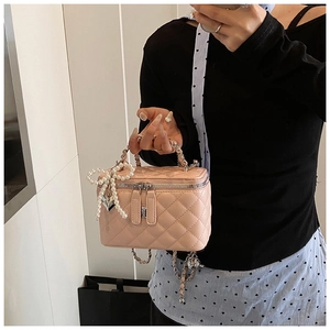Detail van roze gewatteerde doosvormige tas met parelmoeren strik en ketting