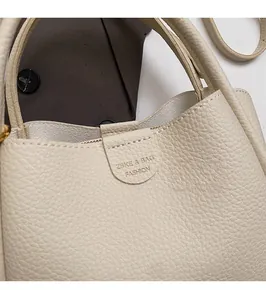 Detail view of cream leather tote bag featuring litchi texture and brand logo embossing