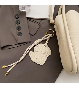 Detail of cream dog charm with gold hardware and woven lanyard on a minimalist bag