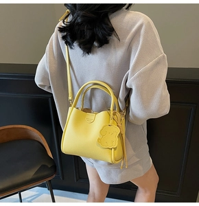Close-up of bright yellow pebbled leather tote with a dog-shaped charm and logo detail
