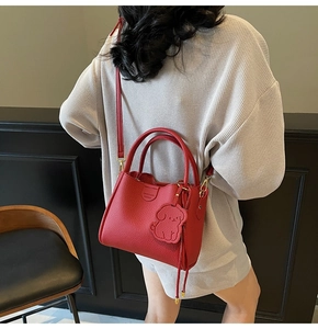 Detailed close-up of a red textured leather handbag featuring a cute dog charm and gold hardware