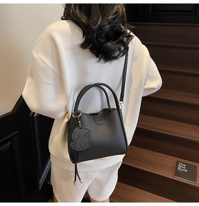 Detail of black lychee leather bucket bag with puppy charm and adjustable strap