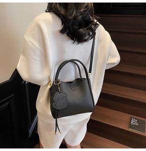Detail of black litchi texture leather handbag with puppy charm and round handles