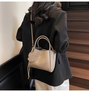Detail of beige lychee grain leather handbag with cute dog charm on stairs
