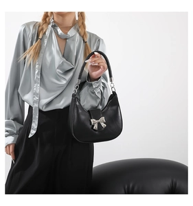 Détail du sac demi-lune en cuir noir avec nœud argenté porté par un mannequin